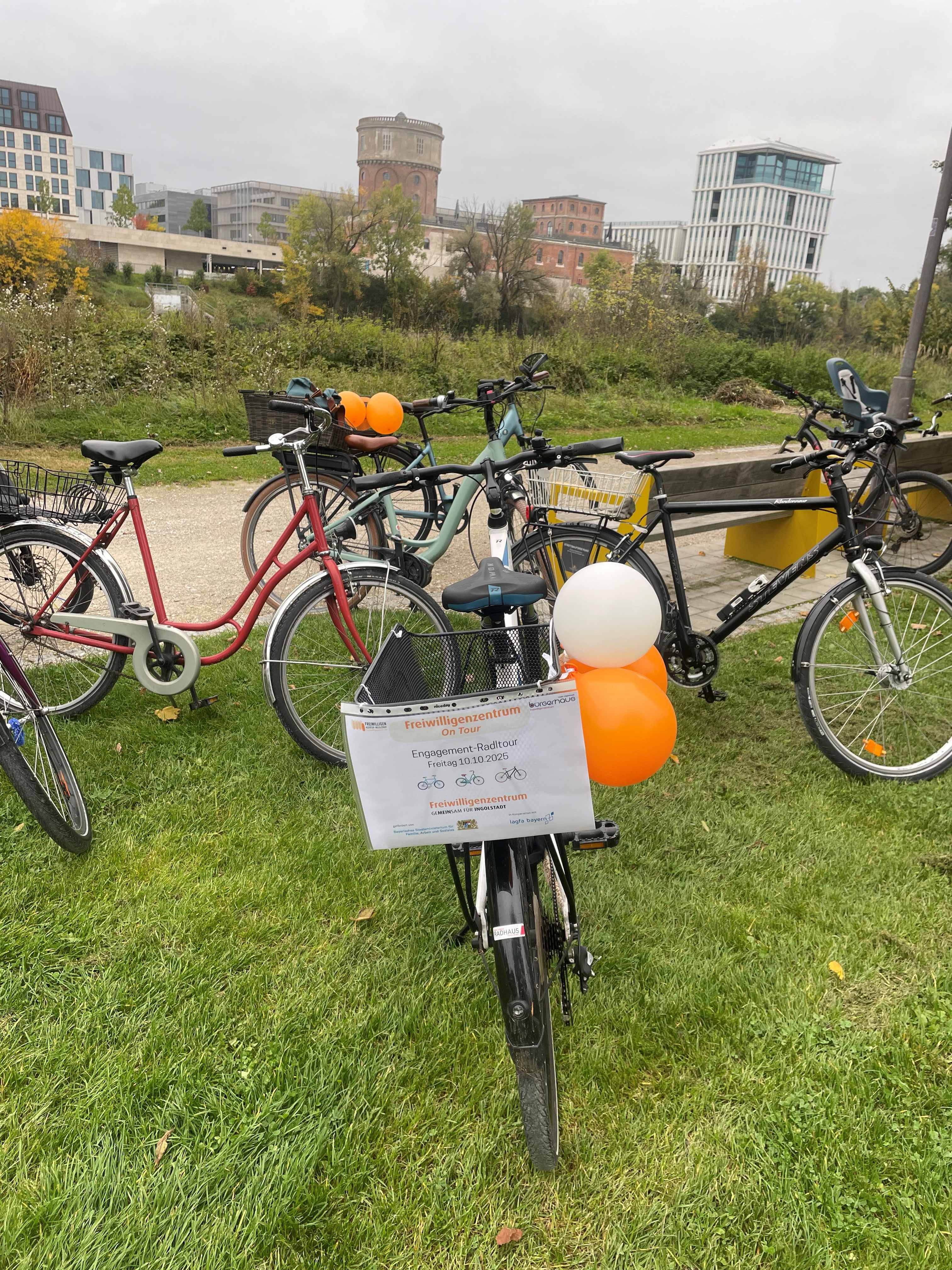 Eine Gruppe von Fahrrädern, eines davon mit Luftballons, steht am Donauufer in Ingolstadt mit Blick auf das Kavalier Dallwigk.